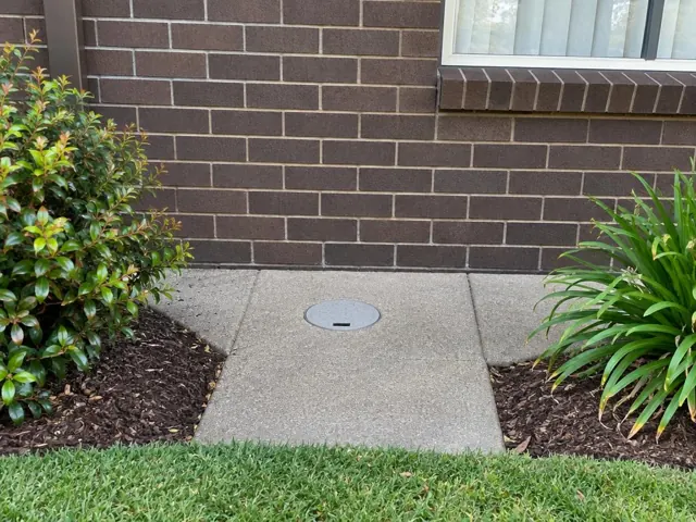 Capped round access point in a reinstated concrete path beside a brick house in Werrington