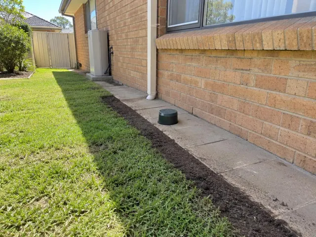Brick house side yard with a capped sewer opening beside concrete paving in Cranebrook